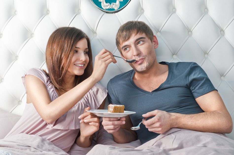 Young lively couple eating cake in their bed