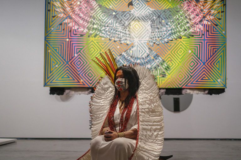 Daiara Tukano during the 34th São Paulo Biennial in 2021, with a painting from the “Dabucuri in Heaven” series. Image by Amazônia Real